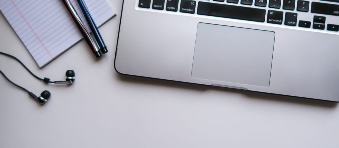 Ear Buds, Two Pens, Small Paper Pad next to Laptop